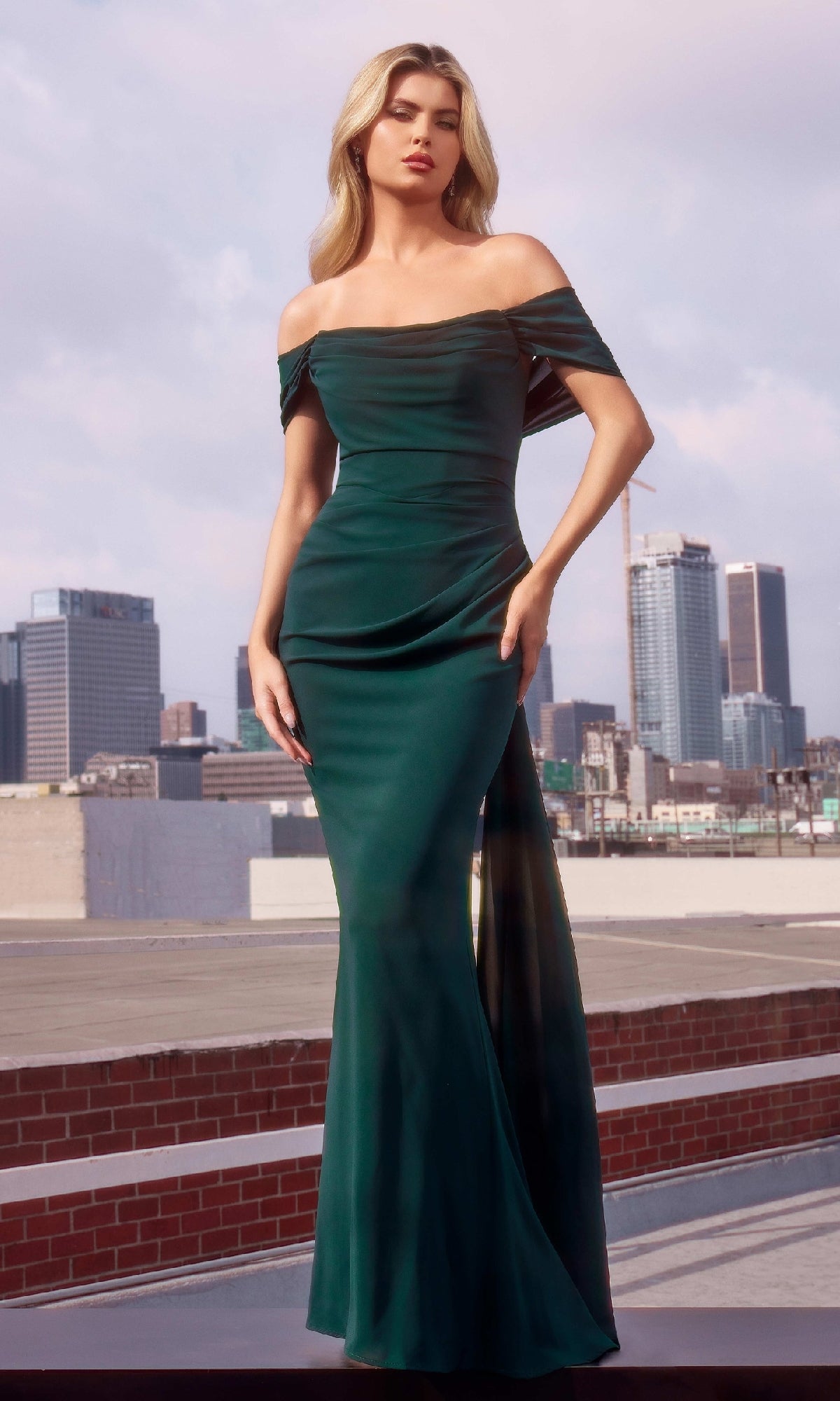 A woman wearing the Ladivine 7433 Multi-Way Long Chiffon Prom Dress in dark green stands on a rooftop, with a city skyline and cranes in the background.